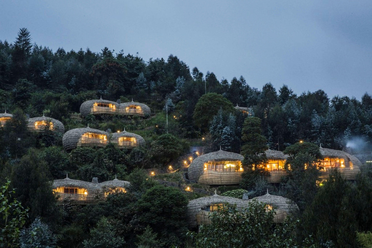 Beleuchtete Villen der Bisate Lodge am bewaldeten Hang in Ruanda bei Abenddämmerung.